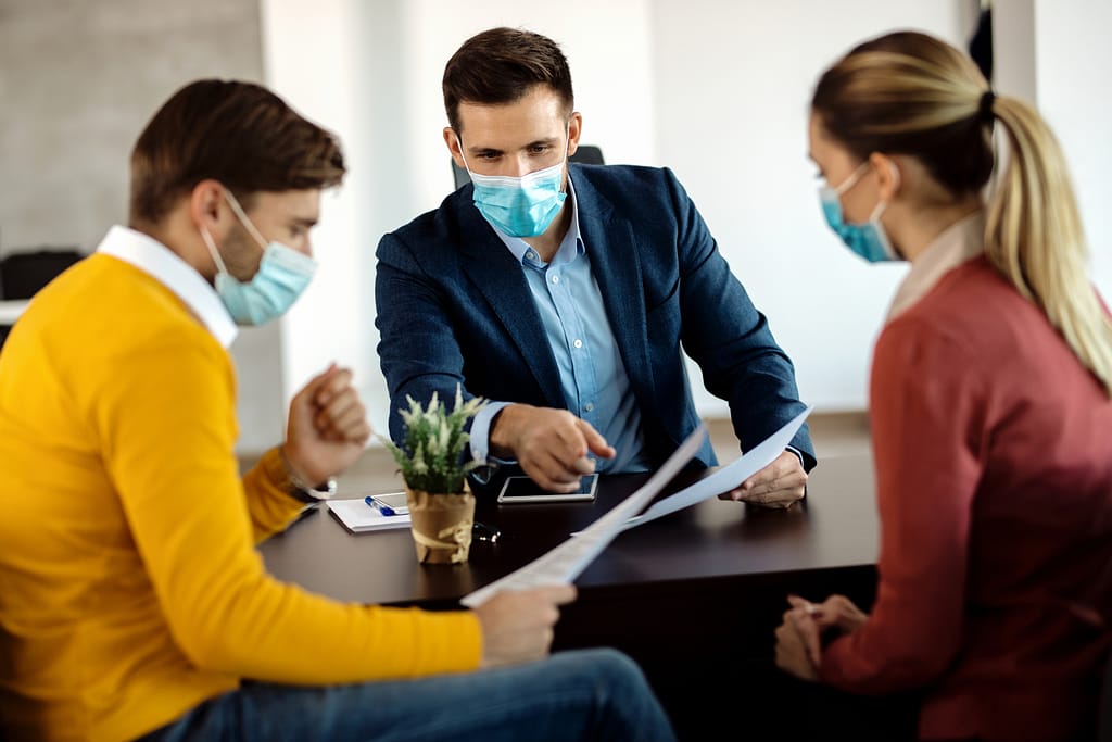 insurance agent couple analyzing documents while wearing protective face masks during meeting scaled What Does Under Contract Mean When Buying or Selling A Home? Lawyer Connection